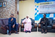 Three people seated on chairs at a book launch event, one speaking into a microphone.